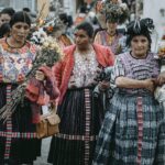 Women in traditional Guatemalan clothing gather with flowers, celebrating a cultural festival.