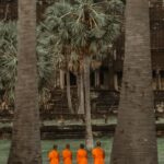 Monks in orange robes stand praying at Angkor Wat, Cambodia, a UNESCO World Heritage site.